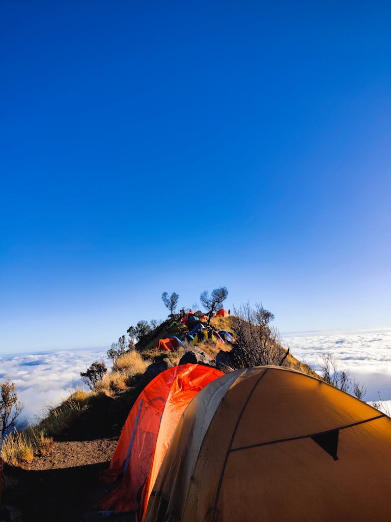 Tents on mountain peak above clouds.